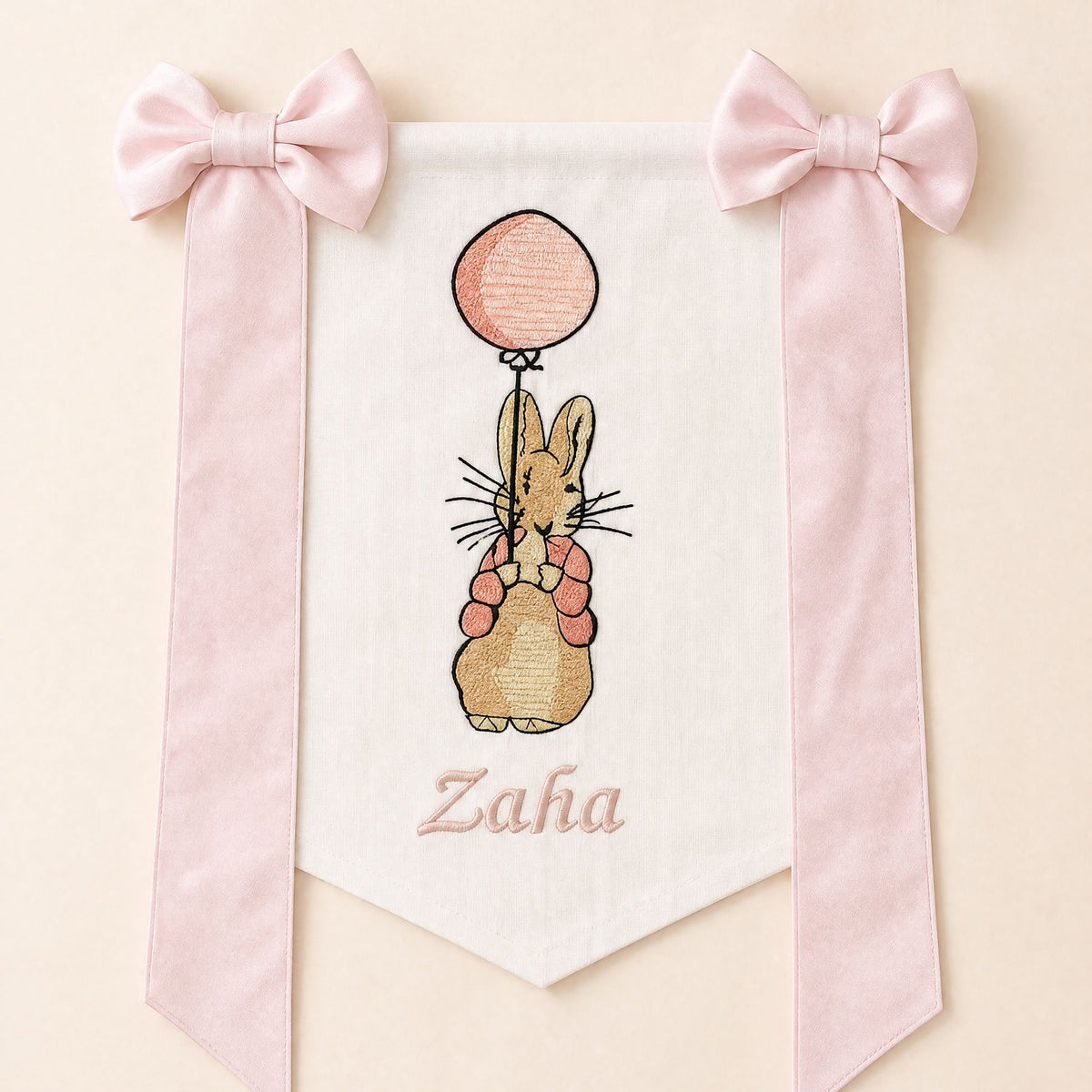 Ivory silk name flag with an embroidered bunny holding a pink balloon, soft pink silk bows and a baby's name in pink script
