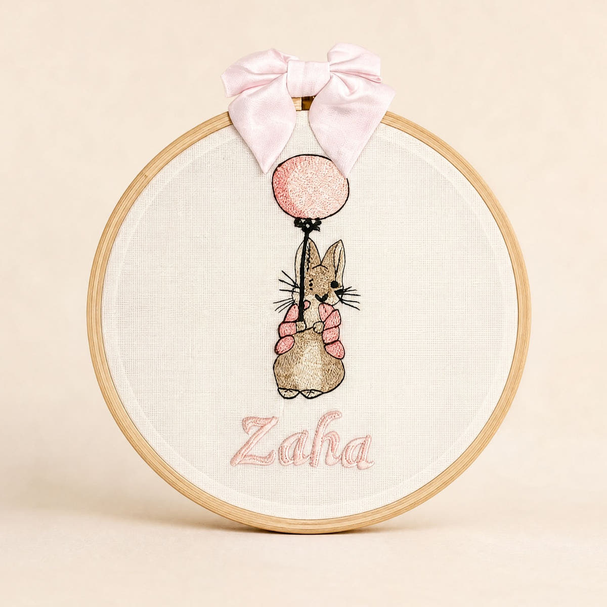 Ivory linen embroidery hoop name frame with a bunny holding a pink balloon, a soft pink silk bow and a baby's name in pink script
