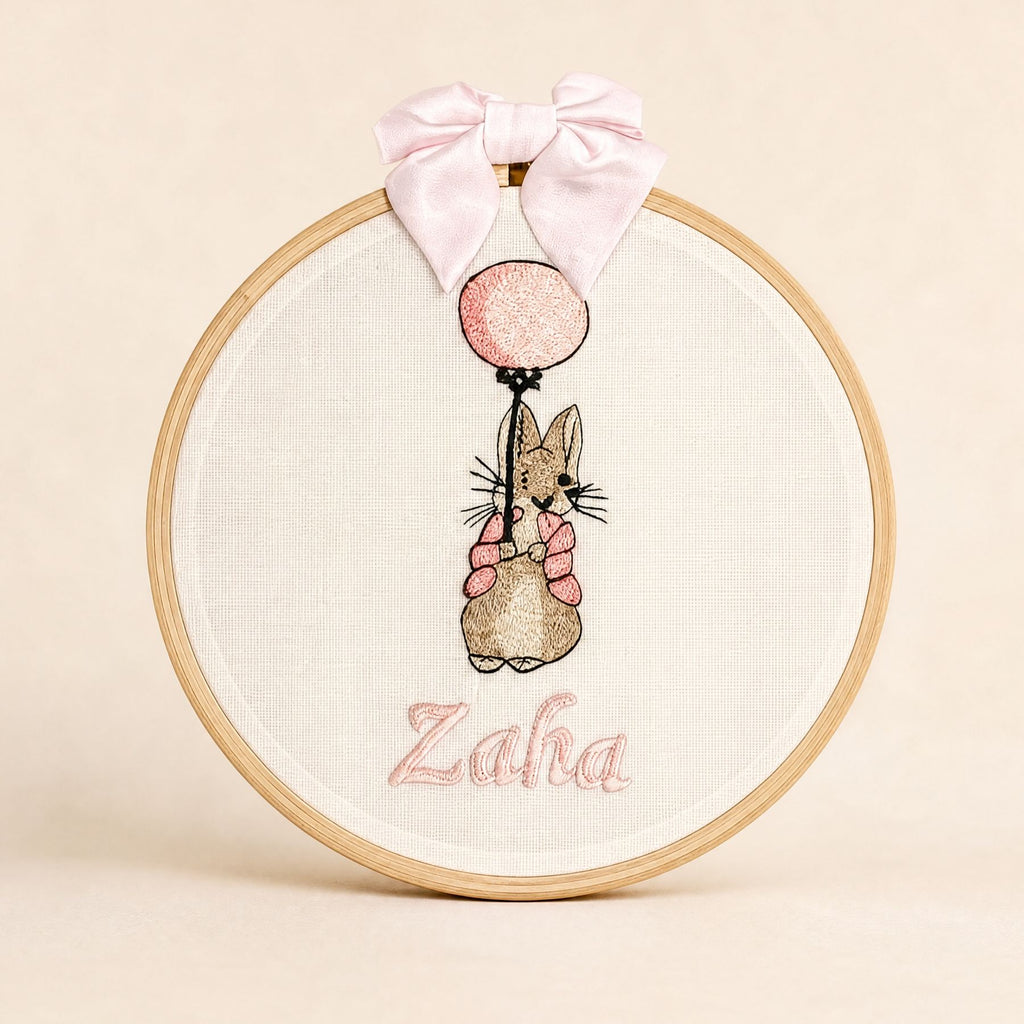 Ivory linen embroidery hoop name frame with a bunny holding a pink balloon, a soft pink silk bow and a baby's name in pink script