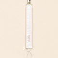 Ivory silk pacifier holder edged in soft pink with a gold clip, cord loop and a baby's name embroidered in pink script