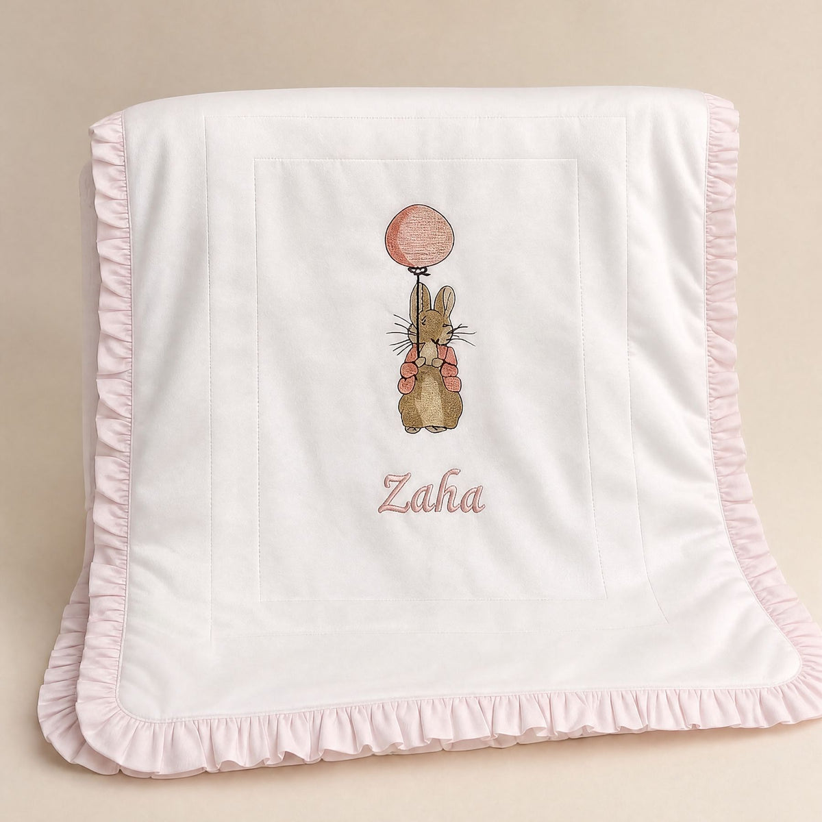 Quilted ivory silk baby wrapping sheet with a soft pink ruffle trim, an embroidered bunny with a pink balloon and a name in pink script