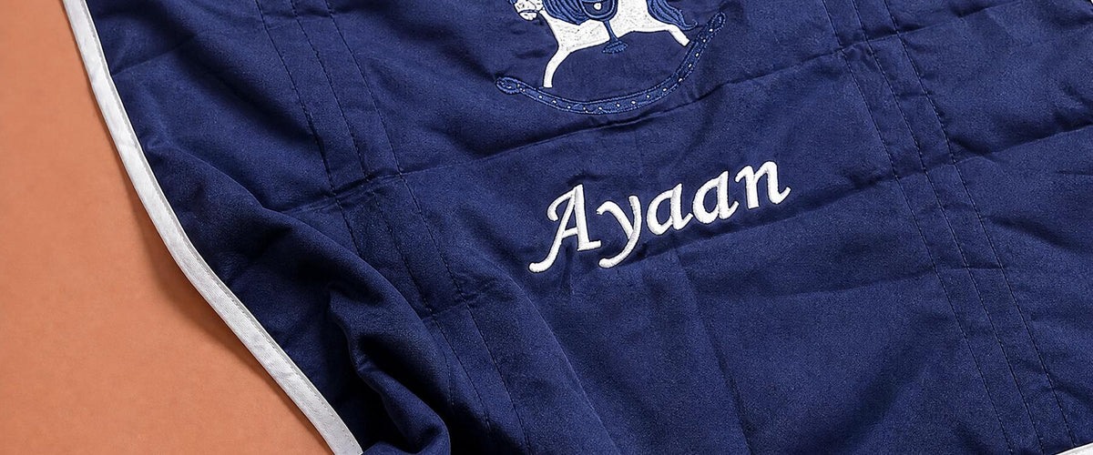 A baby's name hand-embroidered in white on a navy silk wrapping sheet