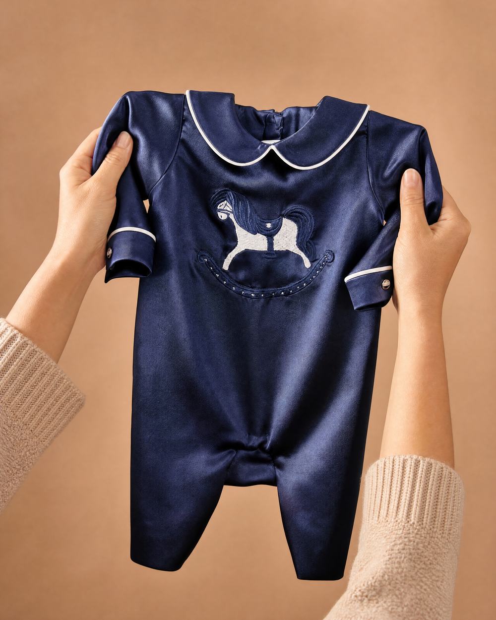 Hands holding up a personalised navy silk Zyra Baby romper